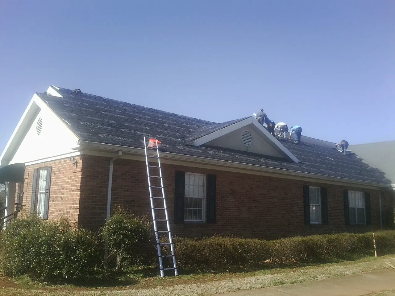Crew tearing shingles off a brick ranch roof with a ladder set — Emergency Roof Repair work by our crew in Meridian